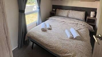A bedroom with a bed, curtains, a headboard, a bedside table, and a wall-mounted shelf.