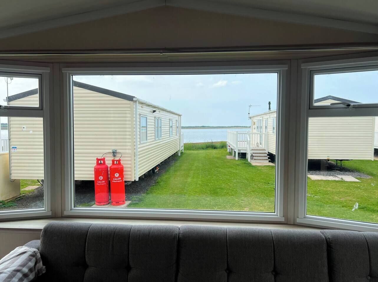 Vue de l’intérieur d’une maison mobile, avec une fenêtre donnant sur une zone herbeuse et d’autres maisons mobiles.