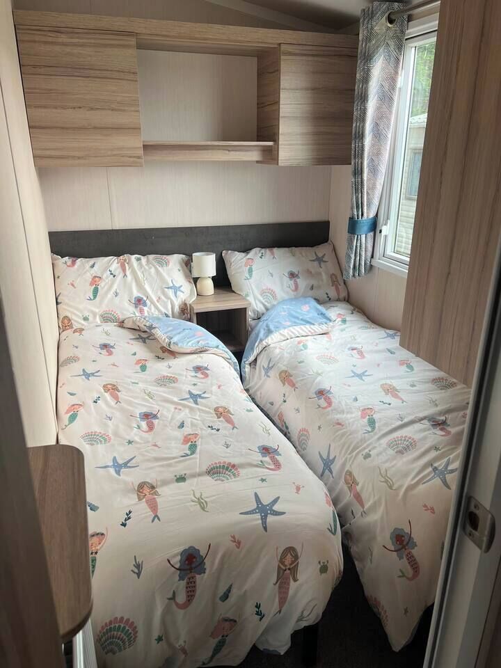 A bedroom with two beds, a nightstand, and a window with curtains.