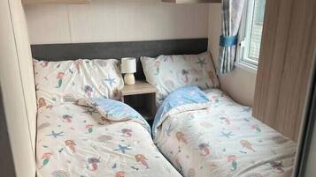 A bedroom with two beds, a nightstand, and a window with curtains.