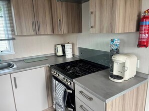 A compact kitchen with a stove, coffee maker, and storage cabinets.