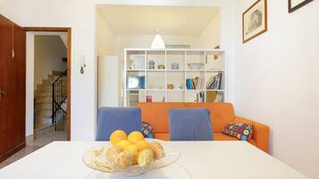 Un comedor con una mesa dispuesta para cuatro personas, una estantería de fondo y una escalera que sube a otro nivel.