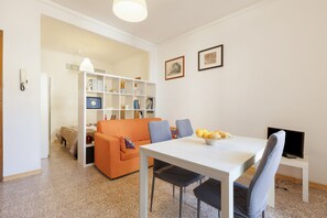 Un espace de vie compact comprenant une table à manger, un canapé, une bibliothèque et un téléviseur.