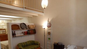 A compact living space with a curved sofa, a small table, a floor lamp, and shelves with various items. - "Ground Floor" Apartment with Wi-Fi, Air Conditioning, and Step-Free Access (Scicli)