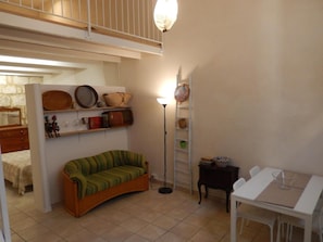 Un espace de vie compact comprenant un canapé incurvé, une petite table, une lampe sur pied et des étagères où sont disposés divers objets.