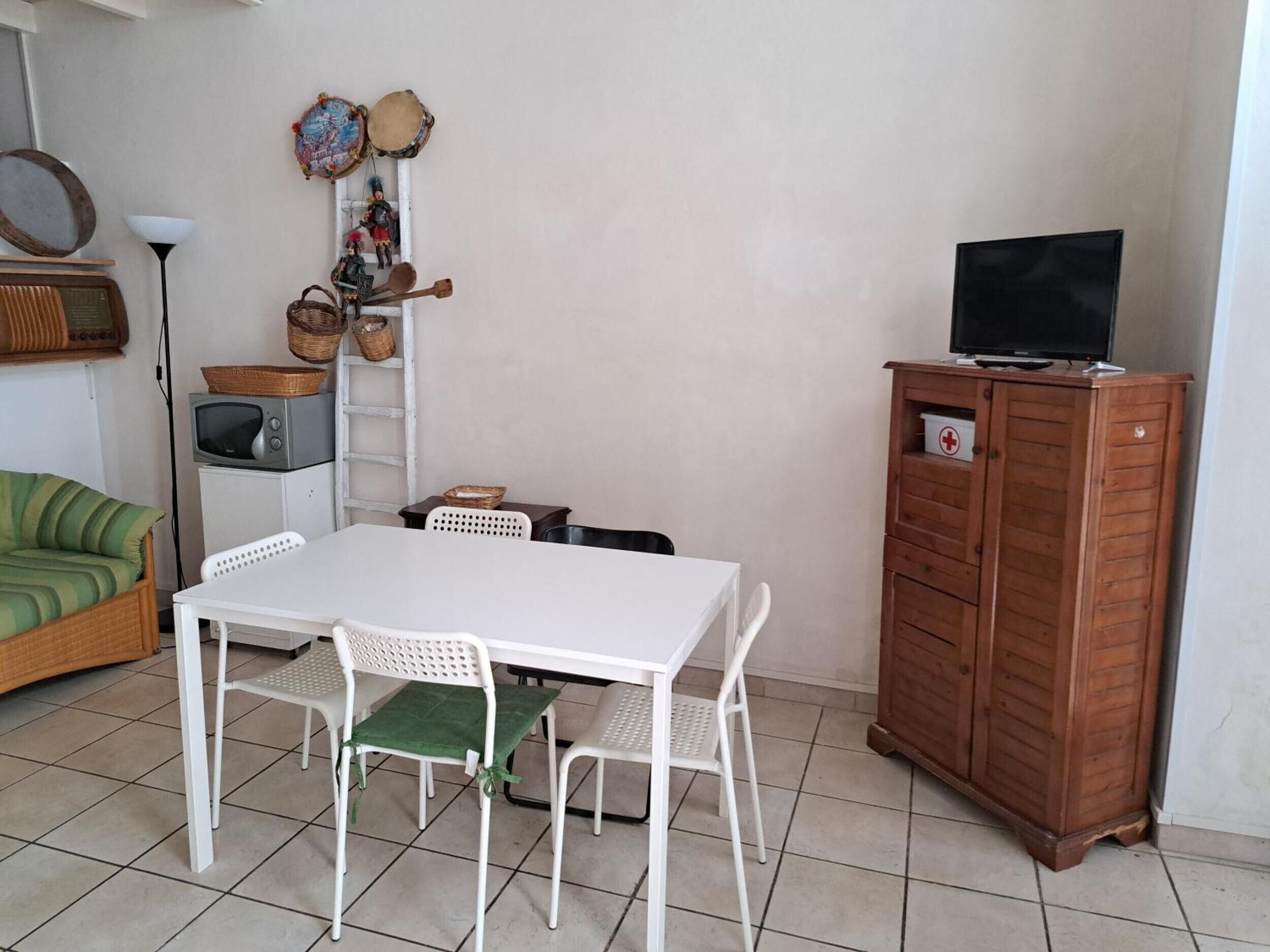 A room with a white table and chairs, a television on a wooden cabinet, and a wicker sofa.