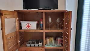 A wooden cabinet with a television on top, containing various items like a first aid kit, glasses, and storage boxes. - "Ground Floor" Apartment with Wi-Fi, Air Conditioning, and Step-Free Access (Scicli)