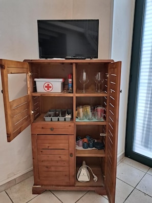 Un meuble en bois sur lequel est posée une télévision, et qui contient divers objets, comme une trousse de premiers secours, des lunettes et des boîtes de rangement.