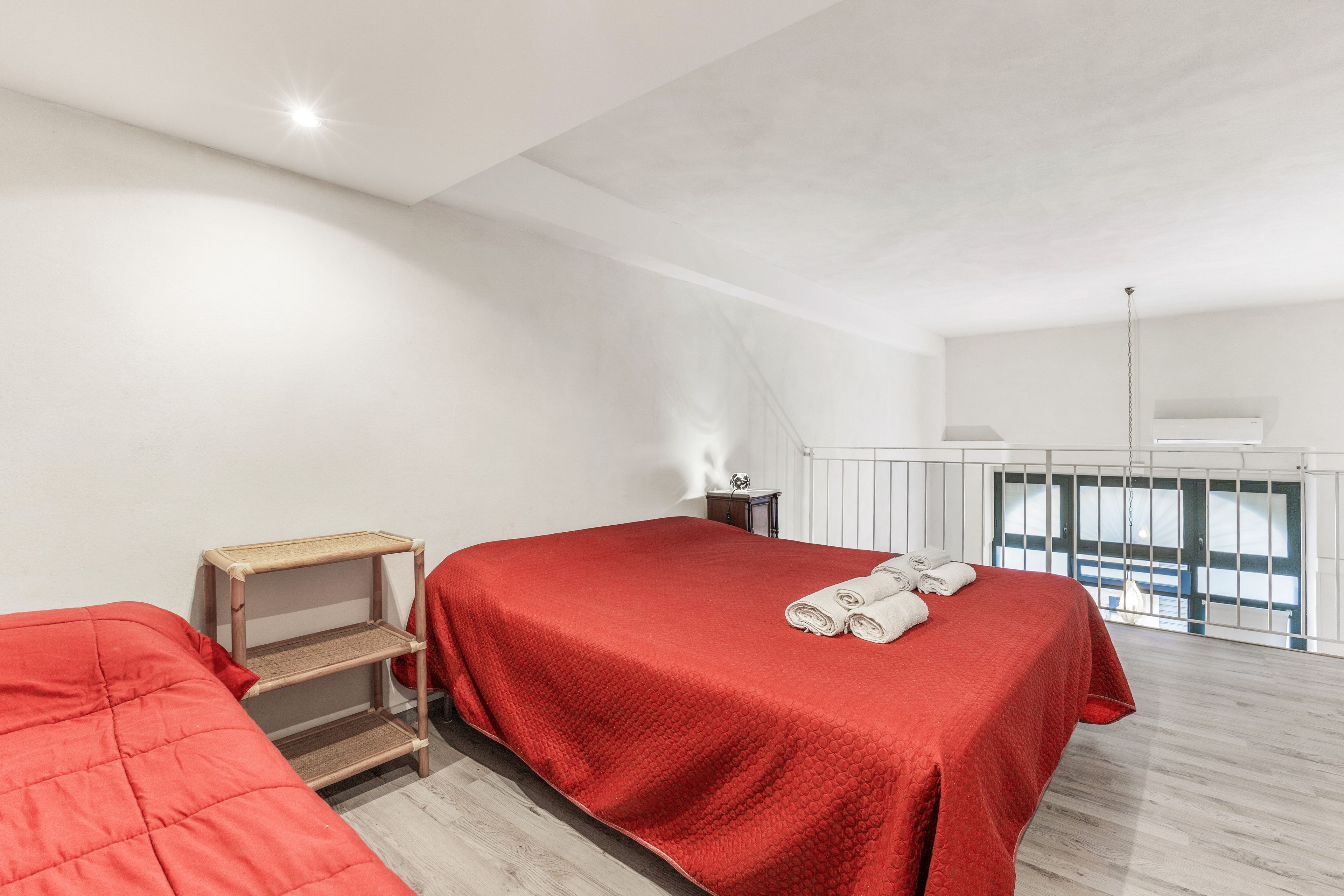 Quarto com colcha vermelha, prateleira de madeira, mesa de cabeceira e janela com vista.