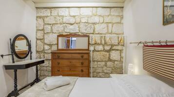 A bedroom with a stone wall, a wooden dresser, a mirror, a bed, and a hanging light fixture.