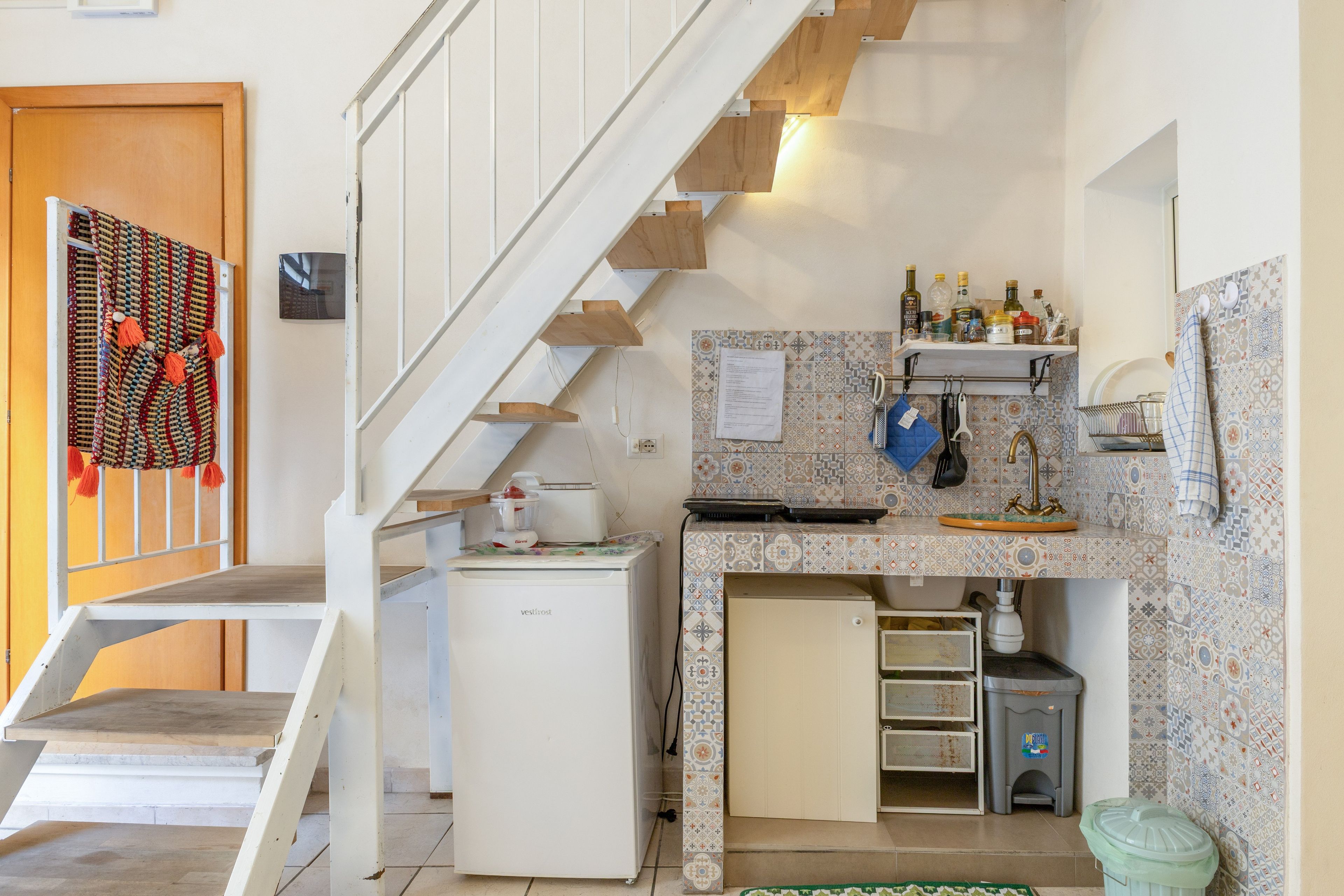 Una cocina compacta con un refrigerador empotrado, un lavamanos pequeño y una escalera de madera.