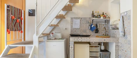 Una cocina compacta con un refrigerador empotrado, un lavamanos pequeño y una escalera de madera.