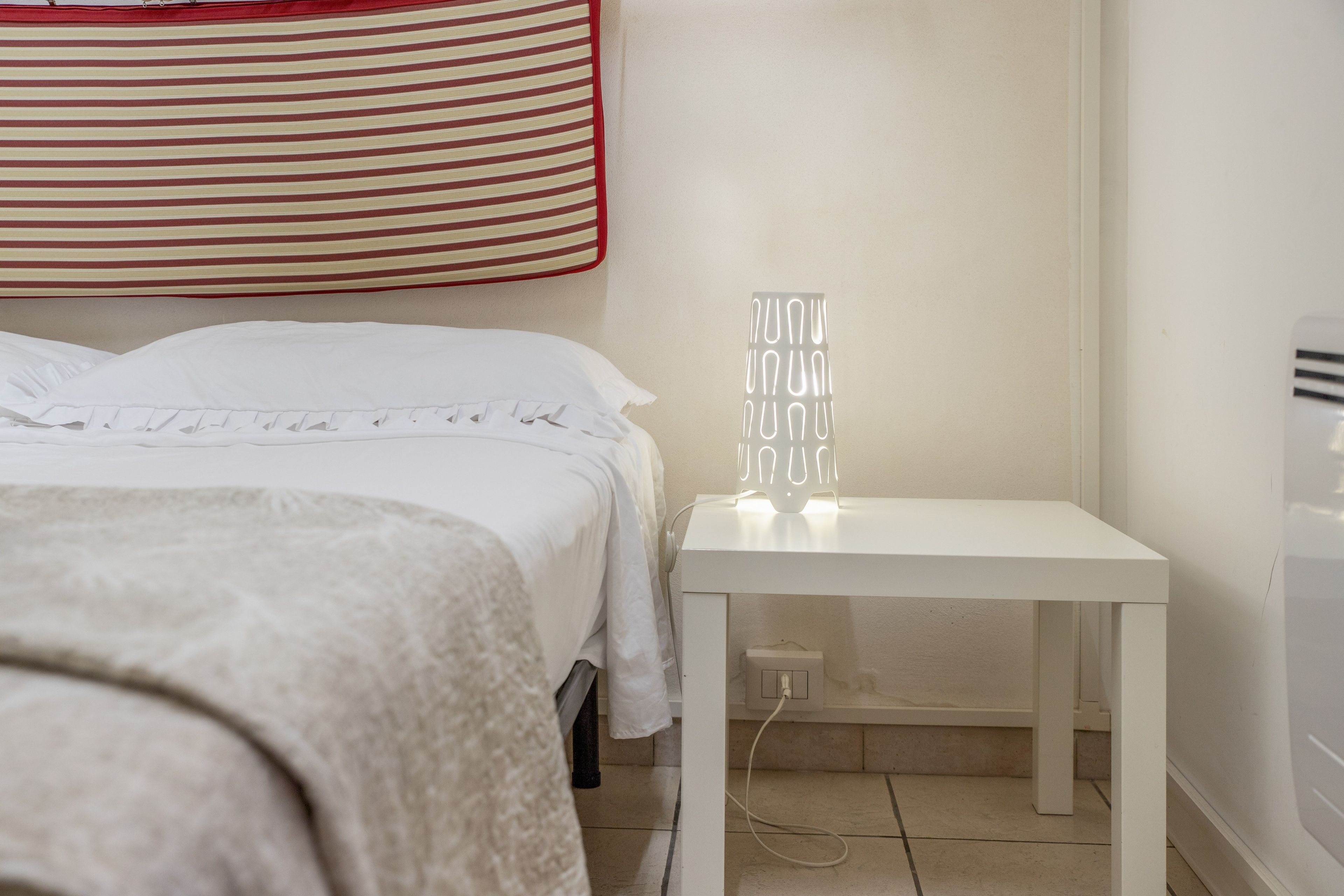 A bedroom with a bed, a bedside table with a lamp, and a wall-mounted light fixture.