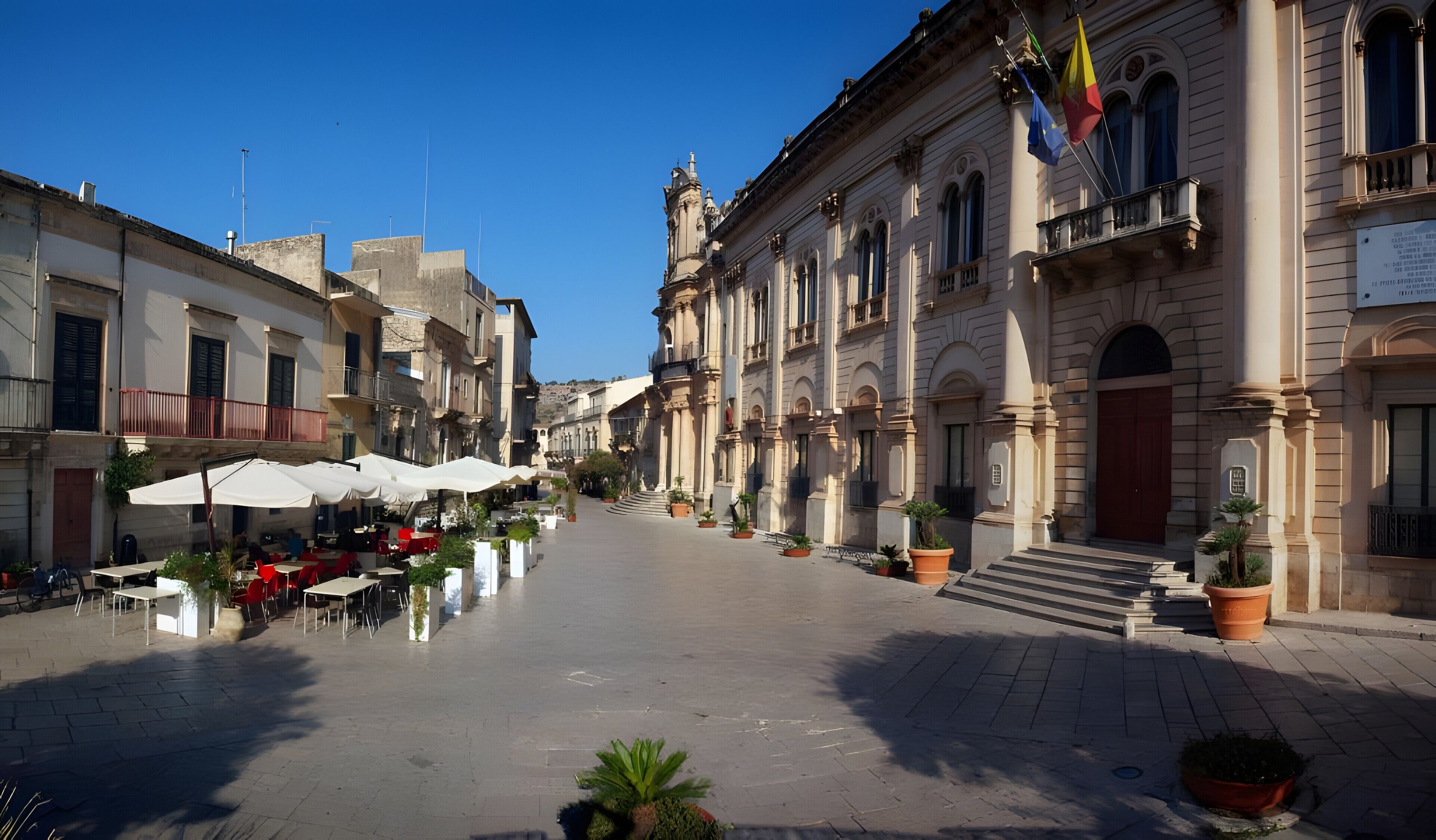 A square with outdoor seating, a building with classical architecture, and a flag.