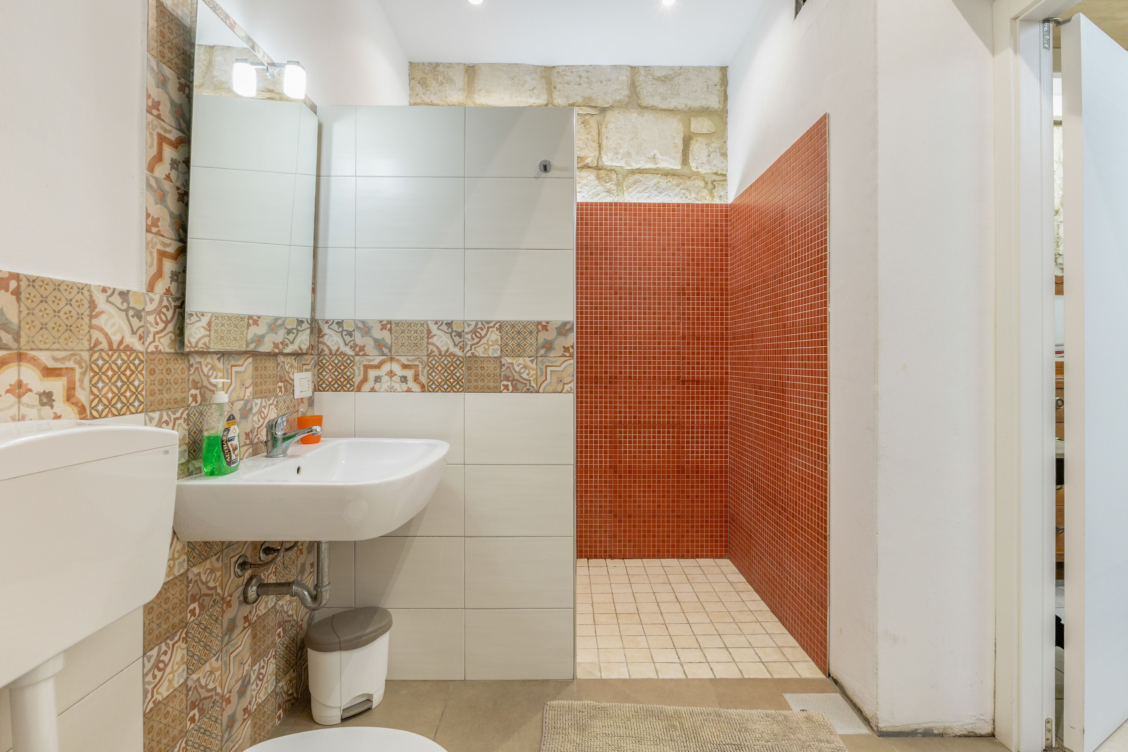A bathroom with a white sink, mirror, and patterned tiles.
