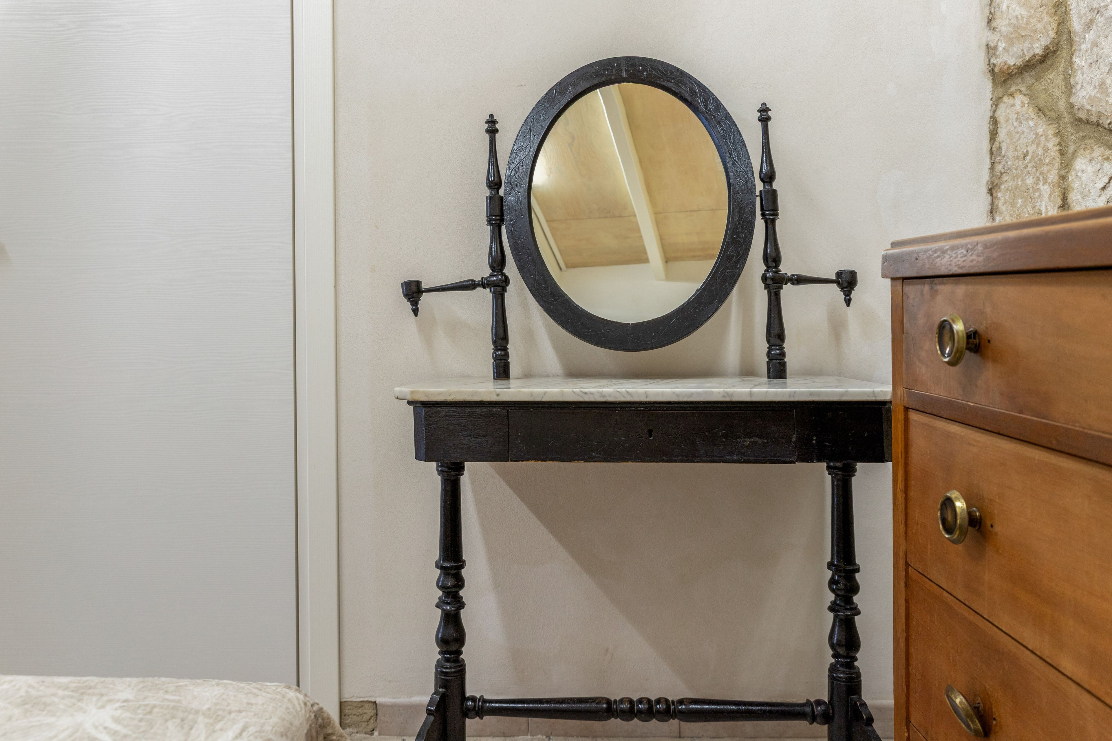 A vintage-style vanity with a round mirror, a marble countertop, and a wooden dresser with brass handles.