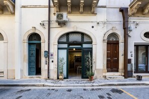 Un edificio con facciata tradizionale, caratterizzato da un ingresso centrale con arco, affiancato da due finestre simmetriche con grate decorative.