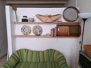 Una habitació amb un sofà verd i ratlles, una estant de fusta amb plats decoratius, un aparell de ràdio i un televisor.