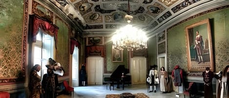 A grand room with ornate ceiling frescoes, a chandelier, and classical furniture.