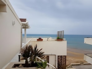 Un balcón con plantas en macetas, vista al mar y fachada blanca de un edificio.