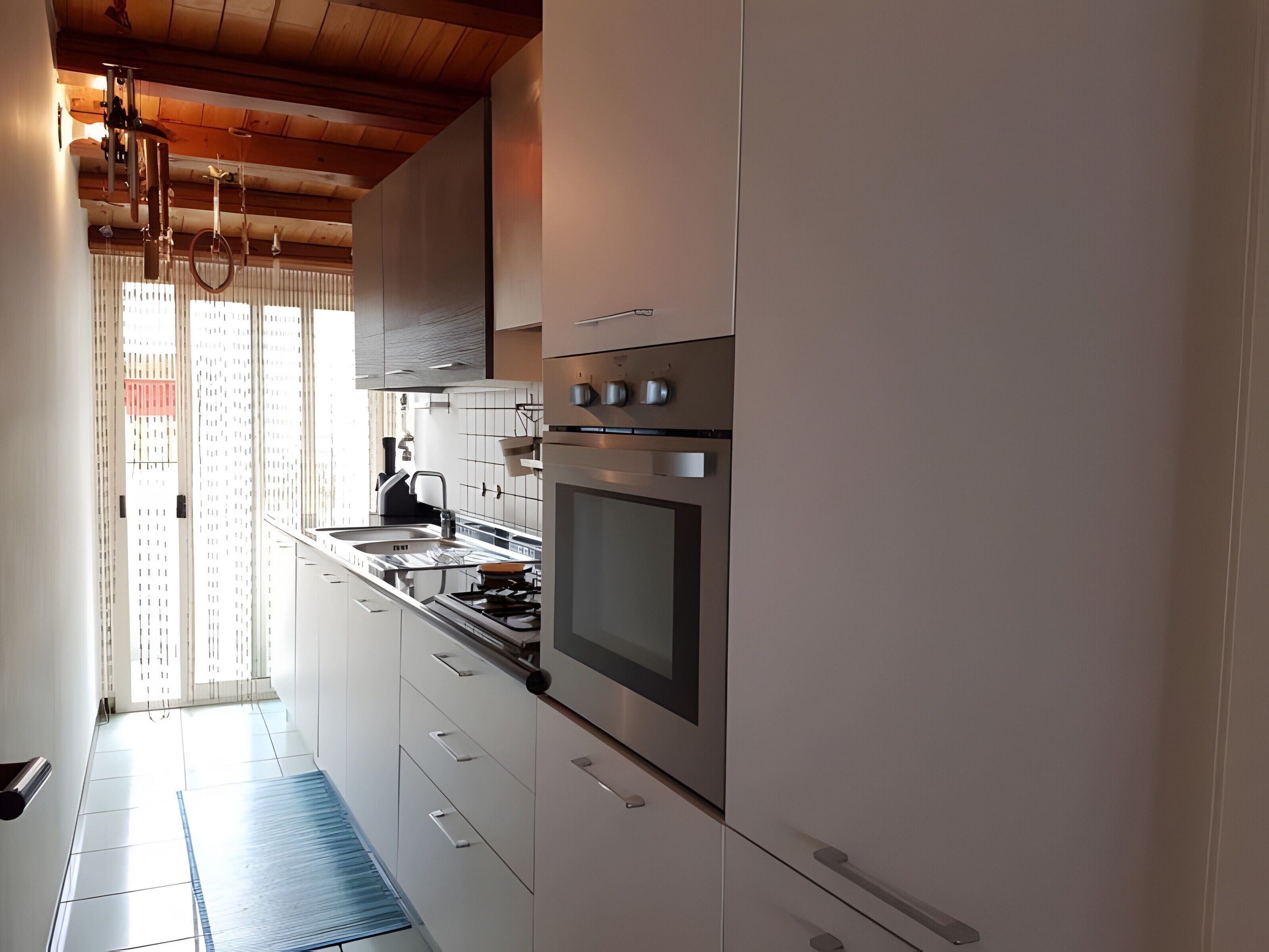 Una cucina moderna con elettrodomestici in acciaio inossidabile, mobili bianchi e soffitto in legno.