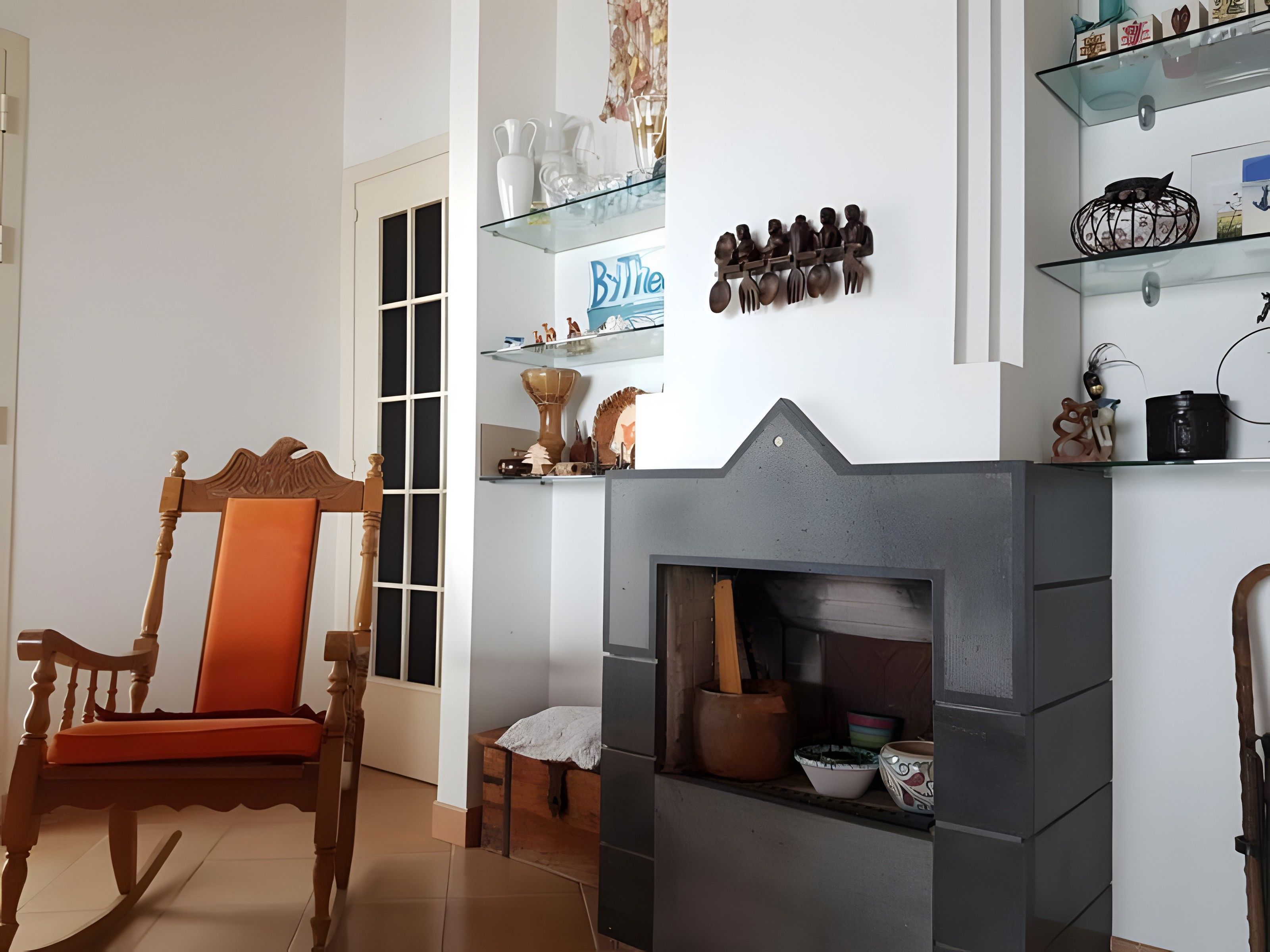 Una sala de estar con chimenea, una mecedora de madera y estantes con objetos decorativos.