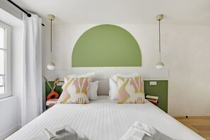 A bedroom with a bed, pillows, a bedside table, a nightstand, a lamp, and a window with curtains. - Two-Bedroom Apartment (Paris)