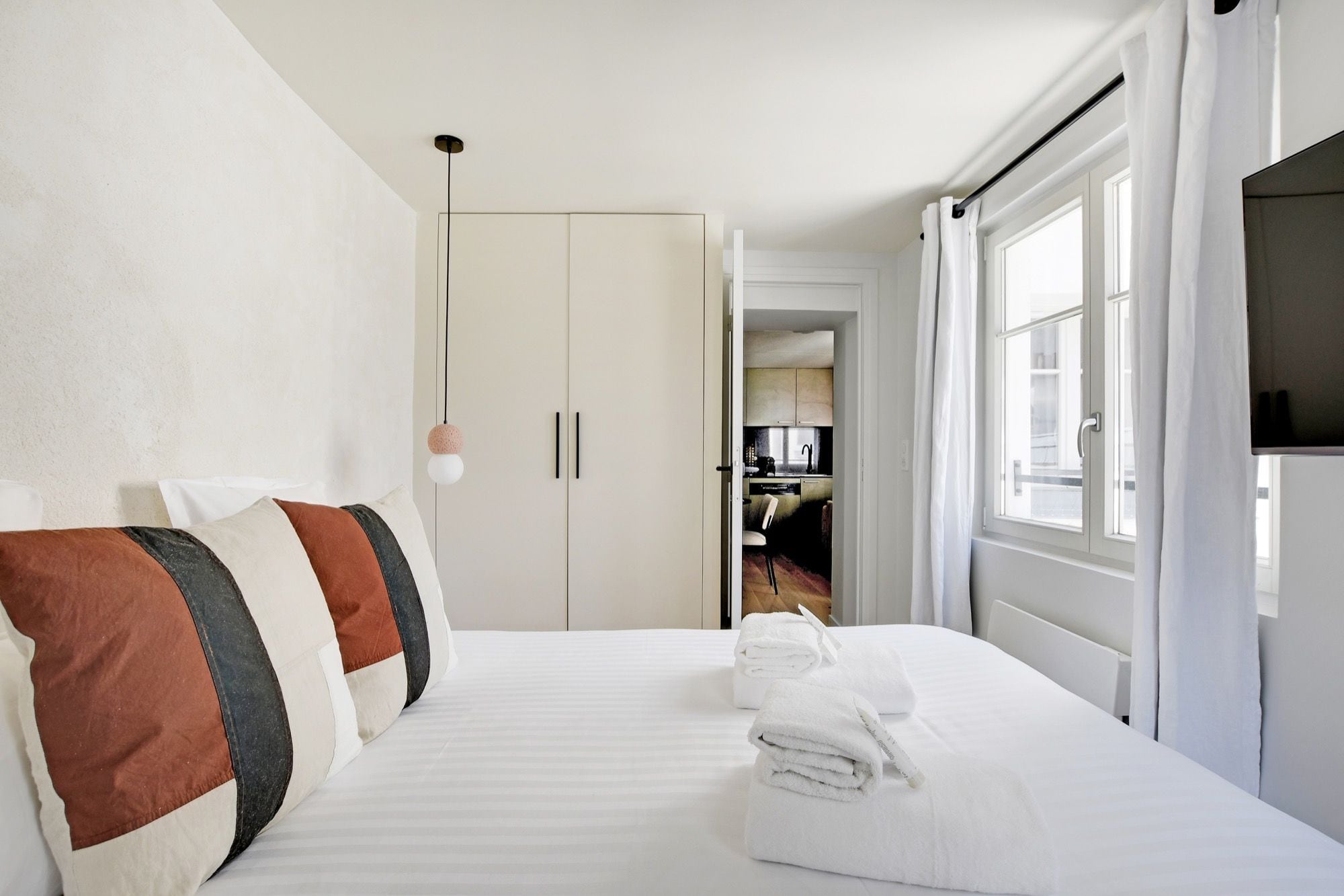 Ein Hotelzimmer mit Bett, Kissen, Fernseher, Kleiderschrank und Blick durch eine offene Tür.