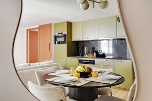 A modern kitchen with a dining area, featuring a round table set for four with plates, cutlery, and a fruit bowl. - Two-Bedroom Apartment (Paris)