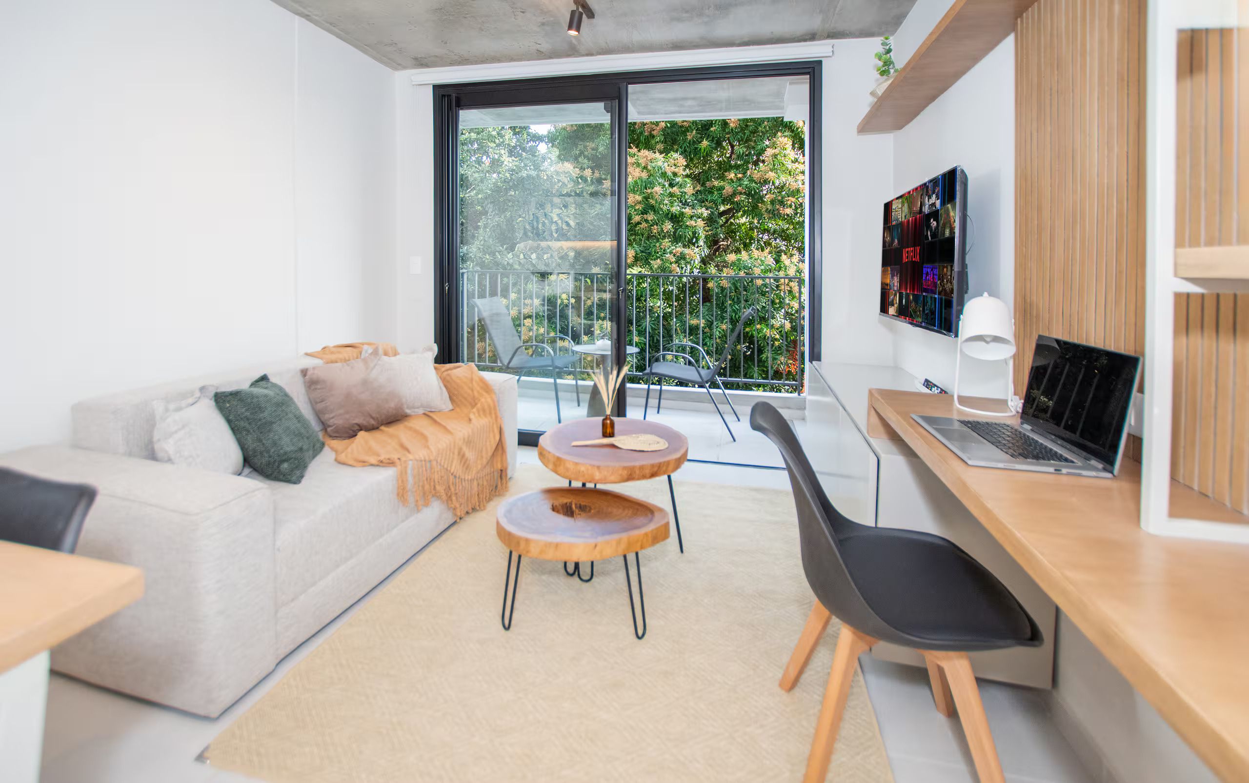 A modern living room with a sofa, two round tables, a laptop, and a TV mounted on the wall.