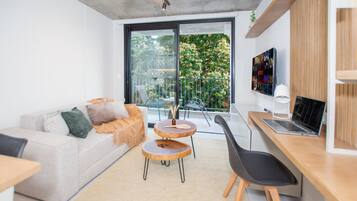 Un salon moderne avec un canapé, deux tables rondes, un ordinateur portable et un téléviseur fixé au mur.
