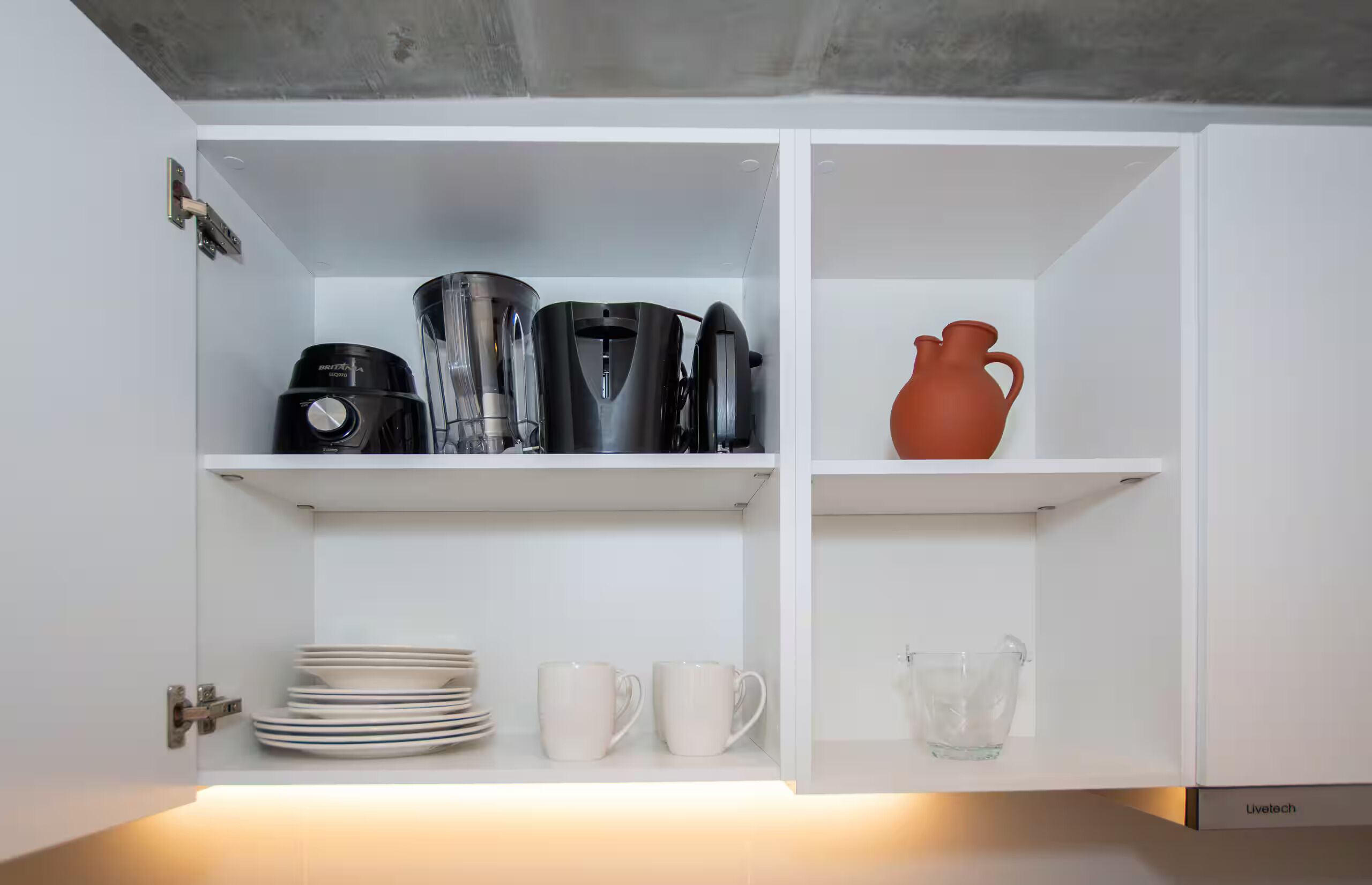 Ein Küchenschrank mit einer Britana-Kaffeemaschine, einem Wasserkocher, einer Stapel Teller und einer roten Karaffe.