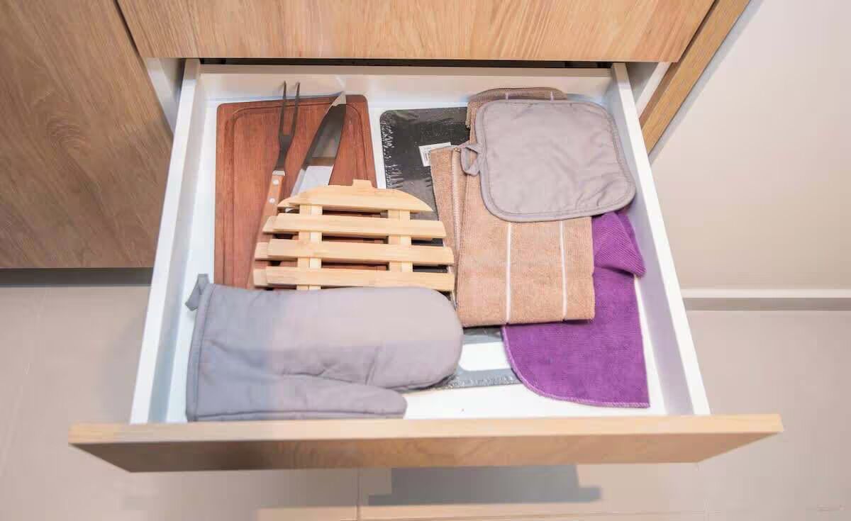 Un cajón con artículos ordenados, incluyendo un perchero de madera, una bolsa marrón, una toalla morada y un objeto negro.