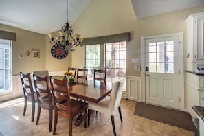 Une salle à manger avec une table et des chaises en bois, un lustre et une vue sur l’extérieur grâce à de grandes fenêtres.