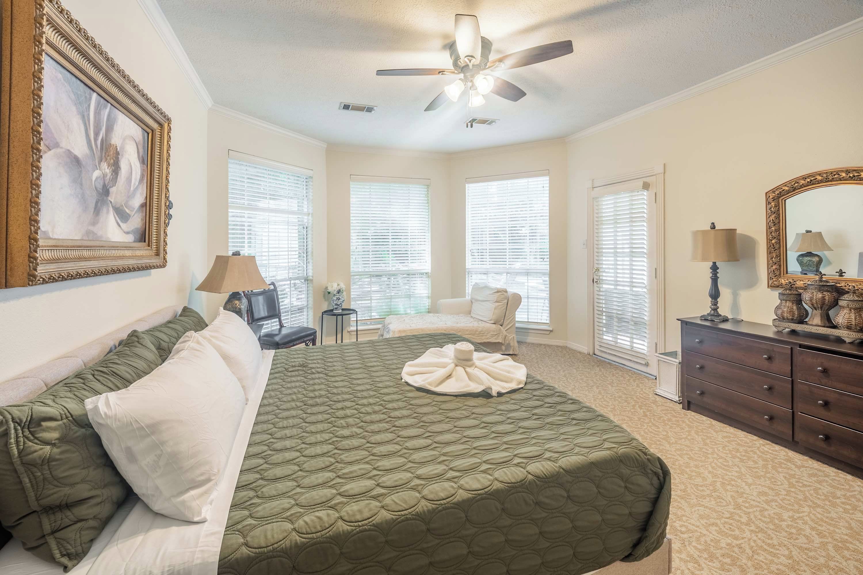 Une chambre à coucher avec un lit, une chaise, une commode et un ventilateur de plafond.