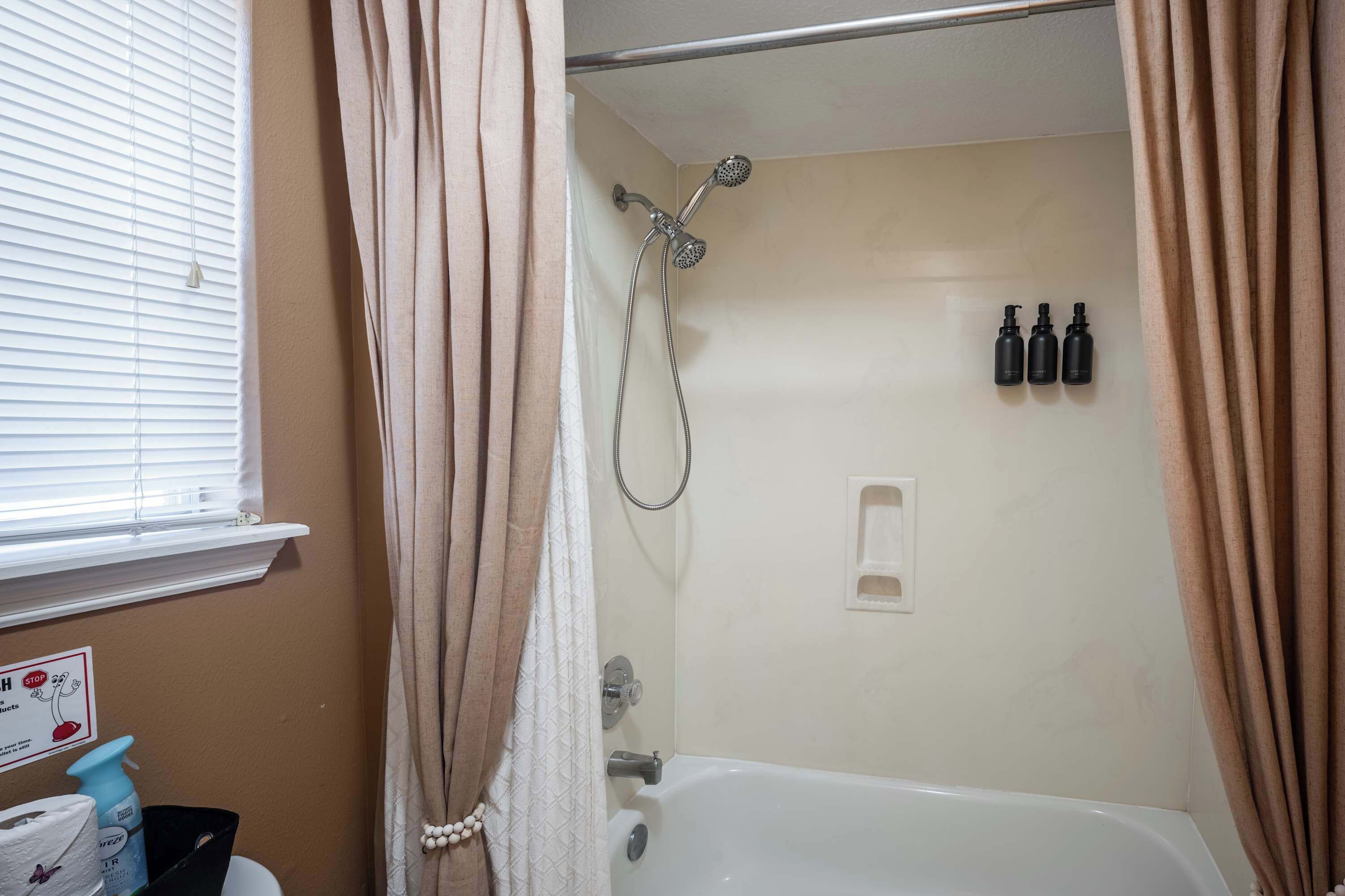 Ein Badezimmer mit einer Badewanne, einer Dusche und drei Shampooflaschen an der Wand.