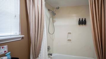 Ein Badezimmer mit einer Badewanne, einer Dusche und drei Shampooflaschen an der Wand.