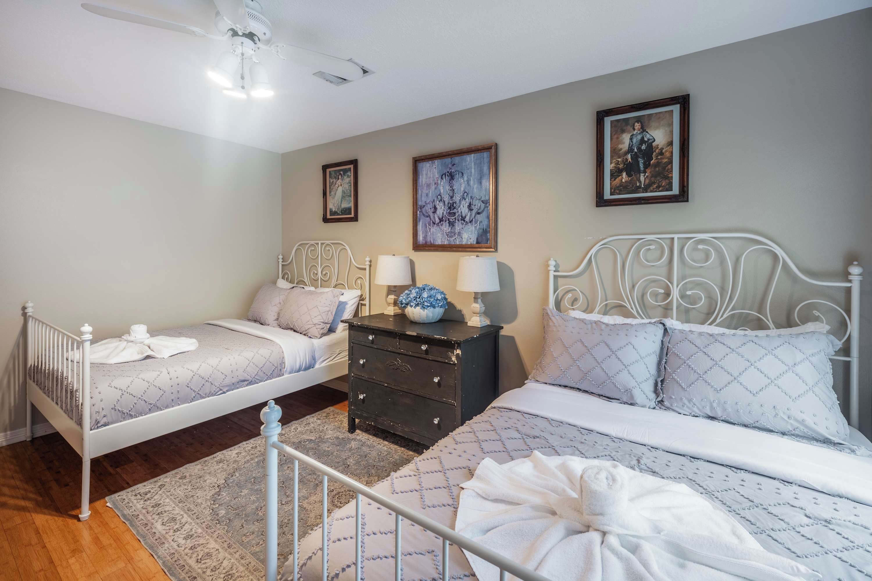 Quarto com duas camas, cômoda e ventilador de teto.