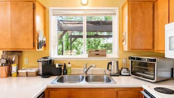 A kitchen with a double sink, a coffee maker, a toaster, and a window with a view of trees.
