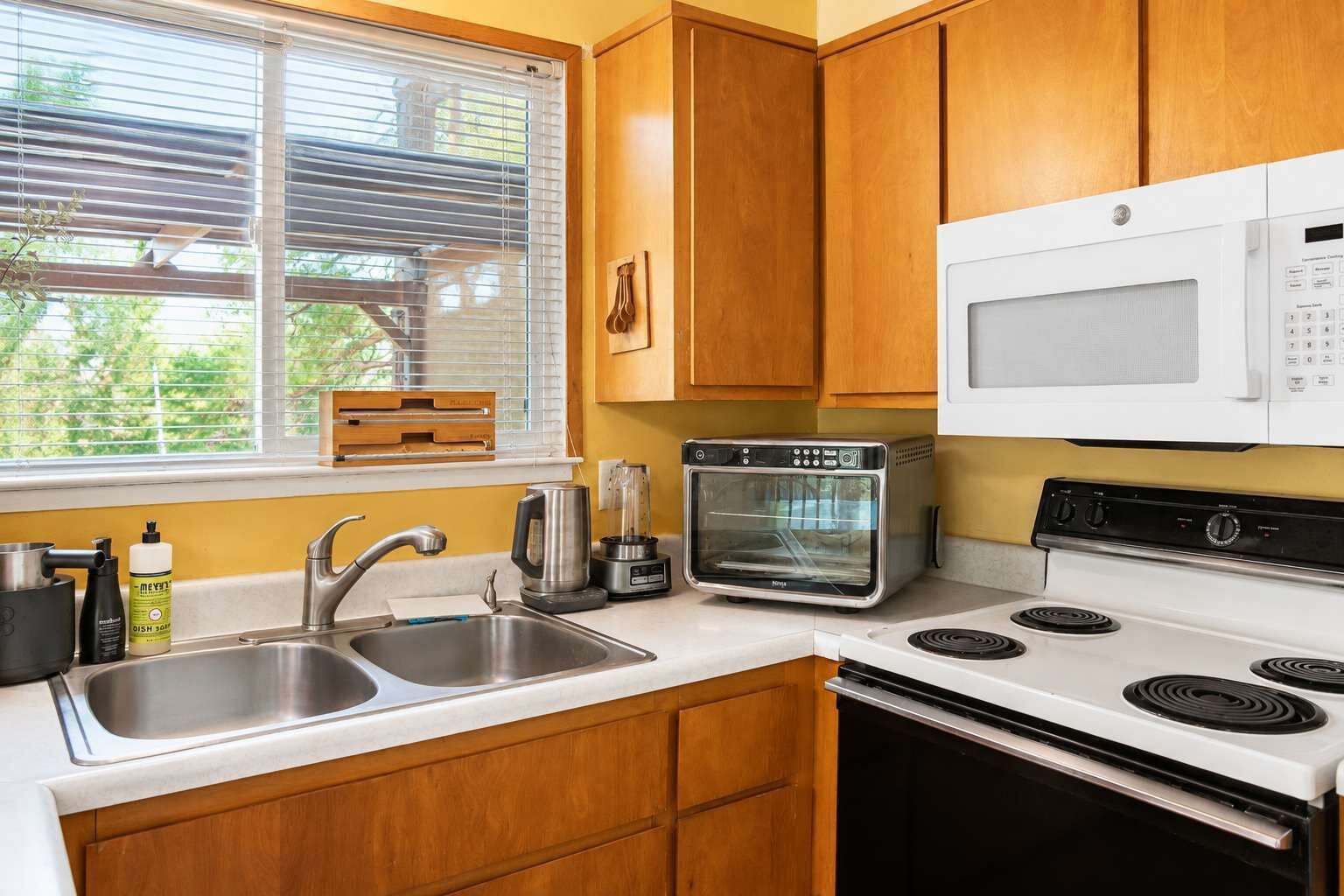 A kitchen with a double sink, a built-in oven, a microwave, and wooden cabinets.