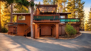 A two-story wooden cabin with a balcony, a covered porch, and a small shed.