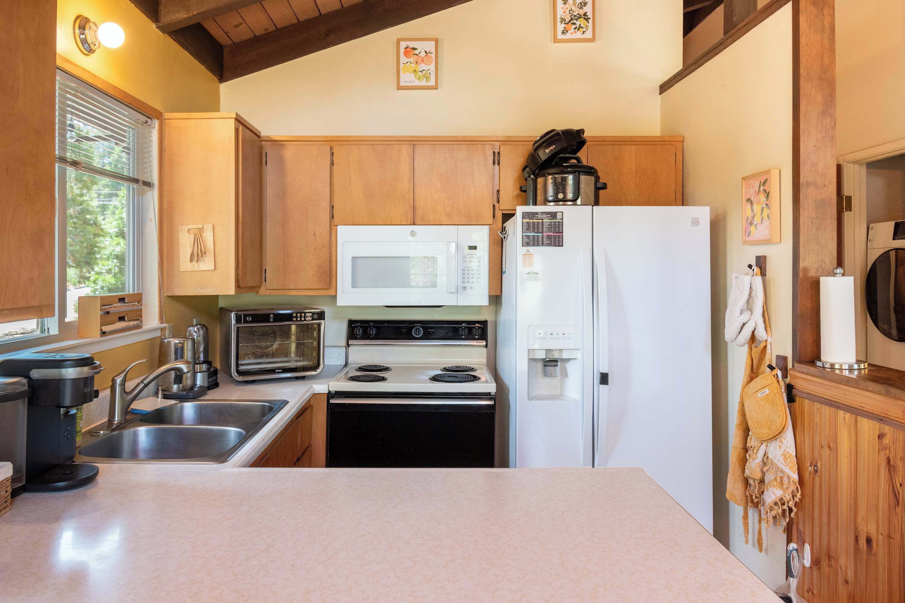Una cocina con armarios de madera, microondas, estufa, horno, pileta y refrigerador.