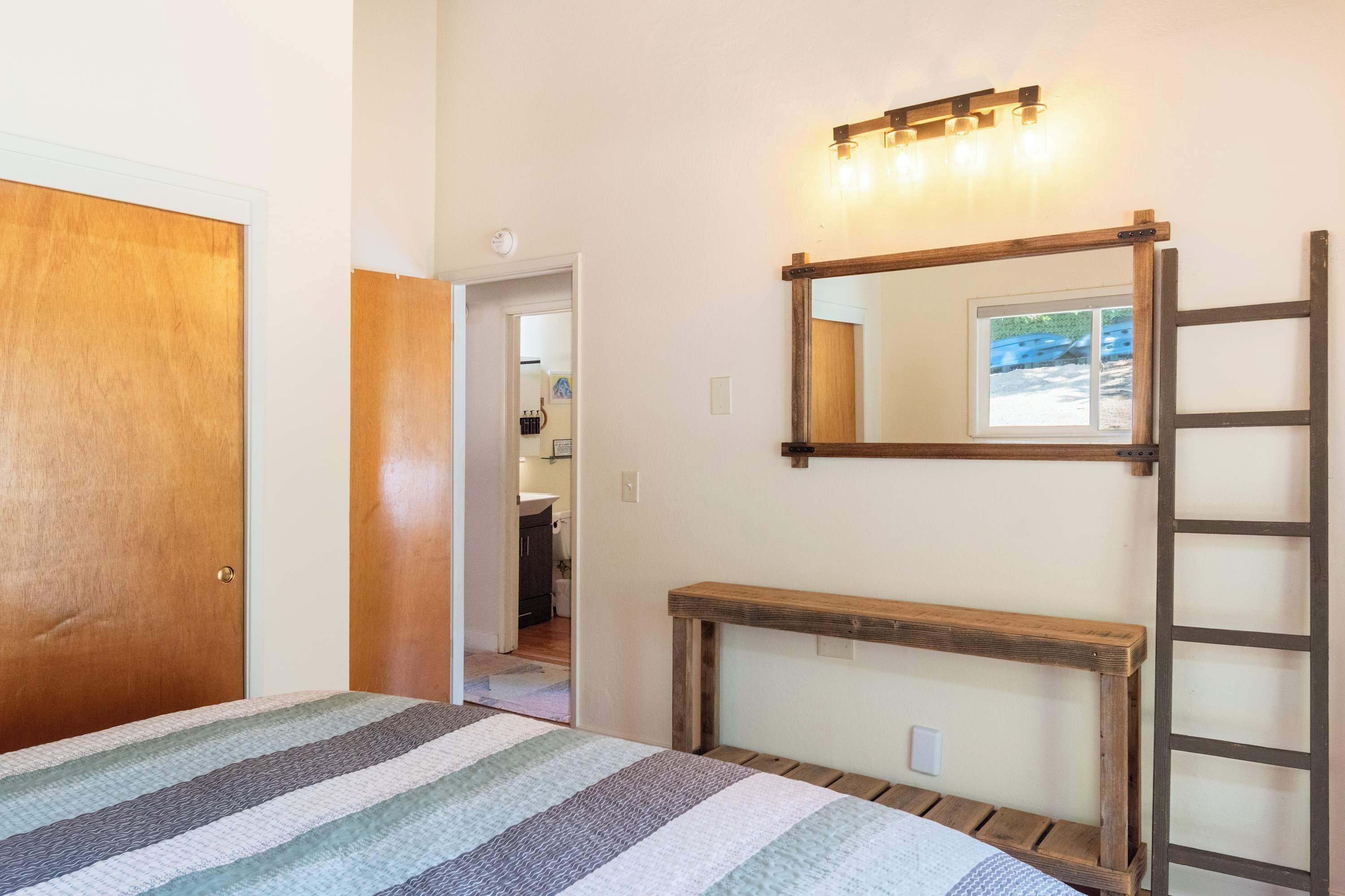 A bedroom with a bed, a wooden bench, a ladder, a mirror, and a light fixture.