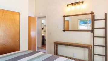 A bedroom with a bed, a wooden bench, a ladder, a mirror, and a light fixture.