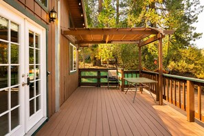 Een houten terras met een pergola, een tafel en stoelen.