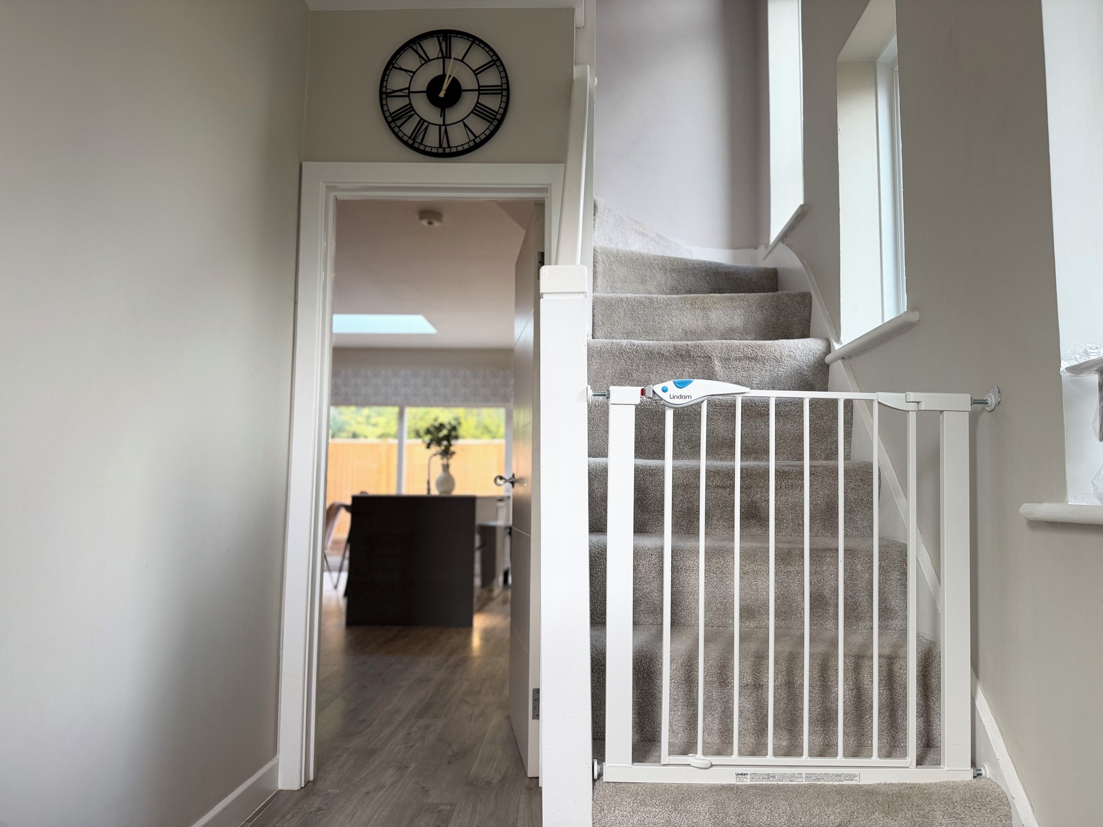 A staircase with a white railing, a clock on the wall, and a view of a backyard.