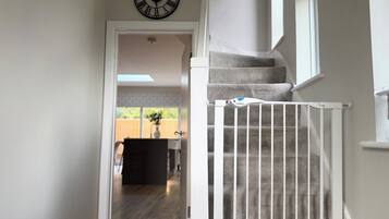 A staircase with a white railing, a clock on the wall, and a view of a backyard.