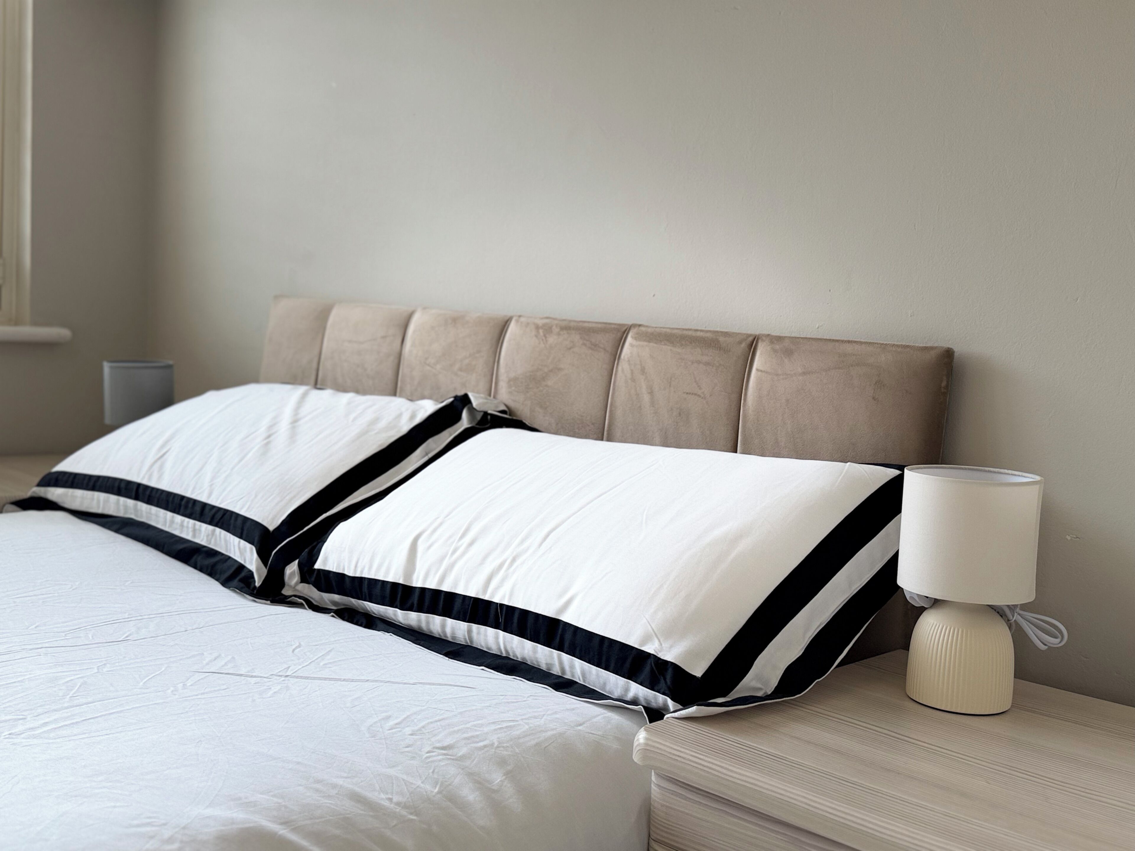A neatly made bed with a headboard, a bedside lamp, and a wall-mounted nightstand.
