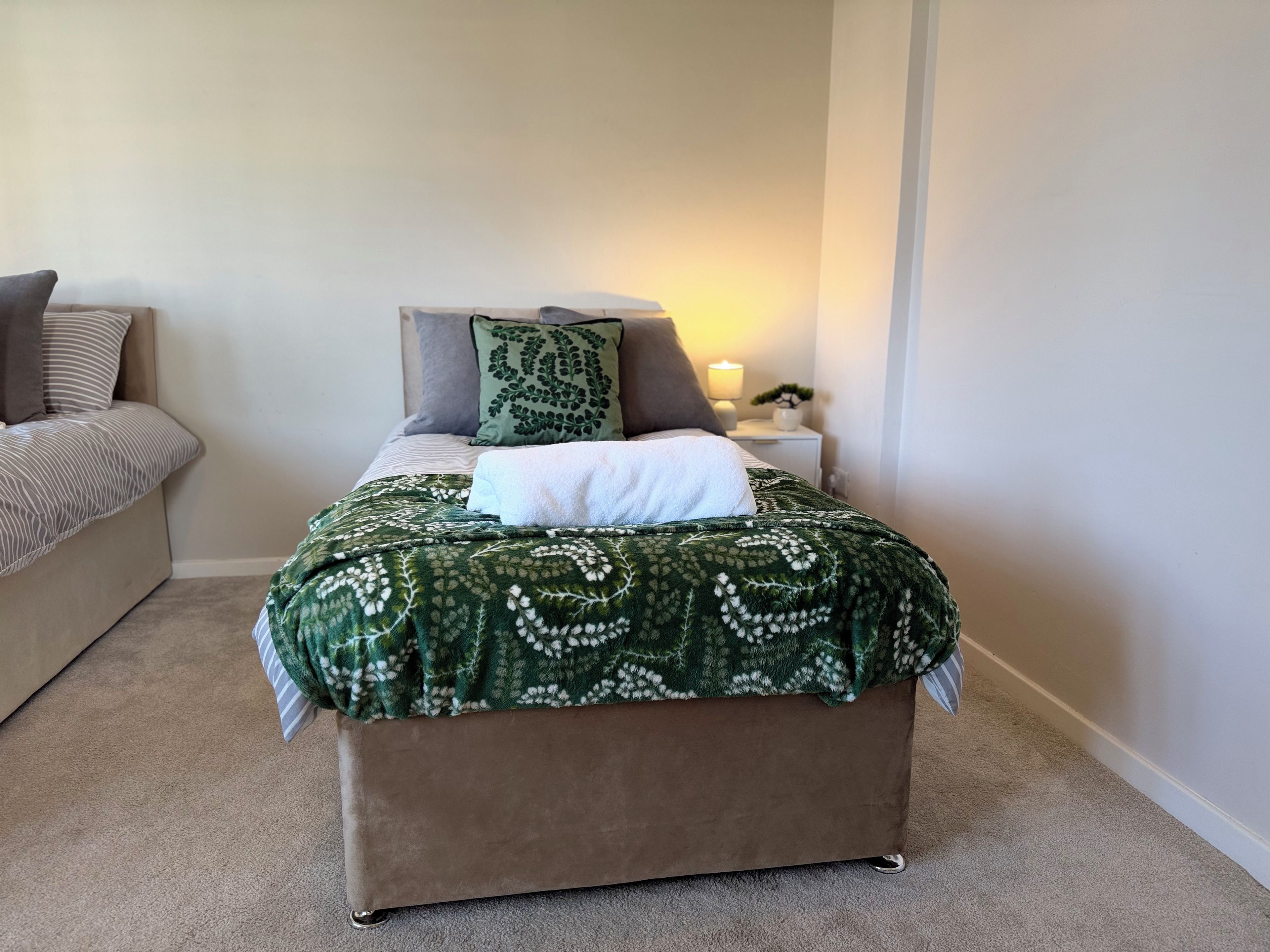 A bedroom with a bed, a nightstand, a lamp, and a small plant.