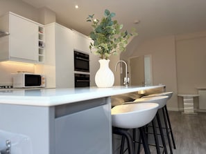 A modern kitchen with a white countertop, a microwave, a white vase with greenery, and a sink with a faucet. - Spacious Family House-Private Hot Tub, Driveway & Easy Access to Beach & London (London)